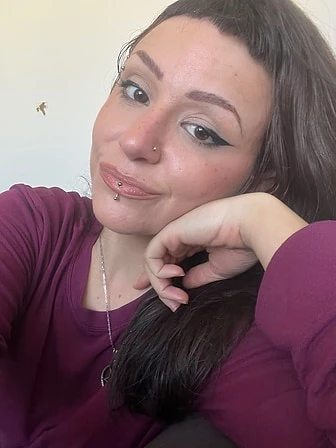 Giovanna, de cabelos longos escuros e blusa vinho, apoiando o rosto na mão.