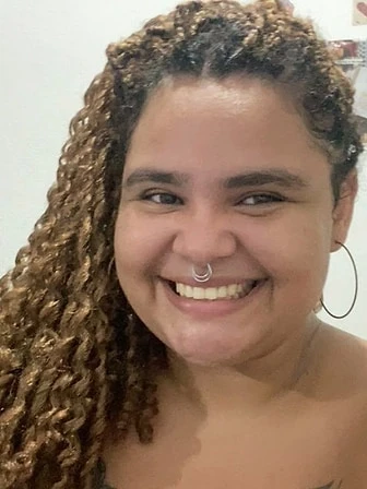 Karen, de cabelos longos cacheados e argola nas orelhas, sorrindo em uma selfie.